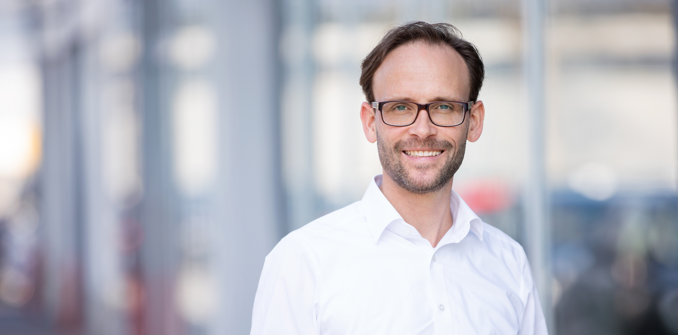 Portrait von Sean Kollak im weißen Hemd vor Glasfassade